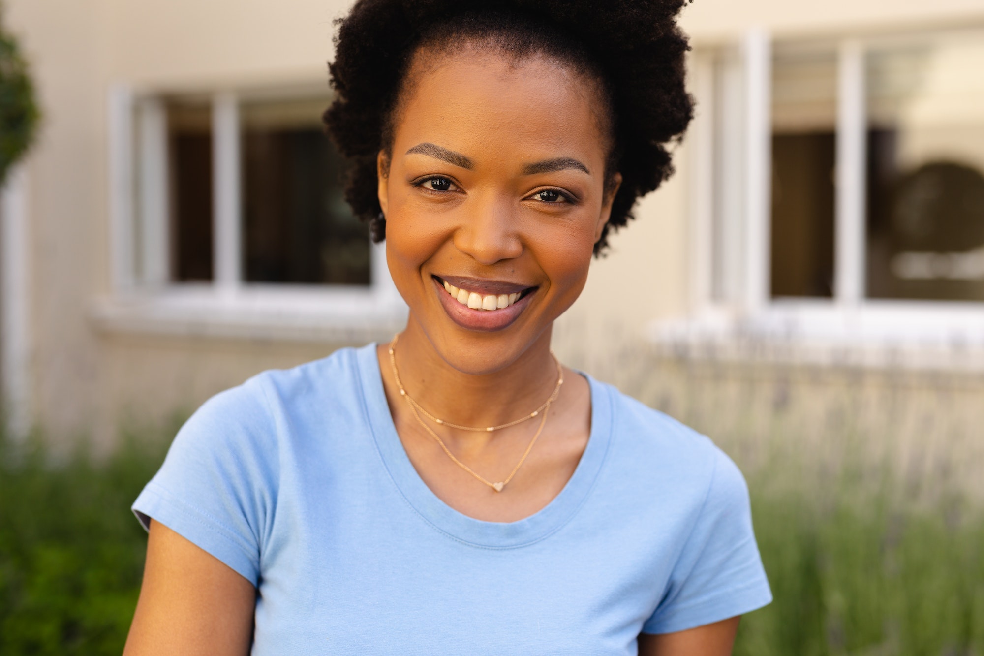 Portrait of smiling african american young woman smiling while standing against house